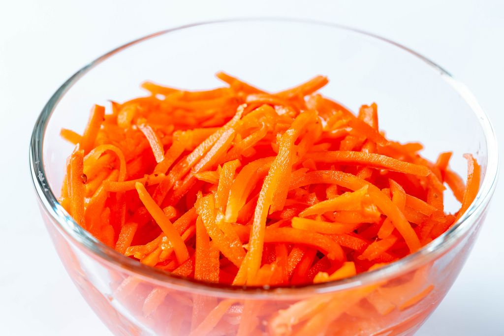 Karottensalat verfeinert mit Gewürzen in Glasschale vor weißem Hintergrund