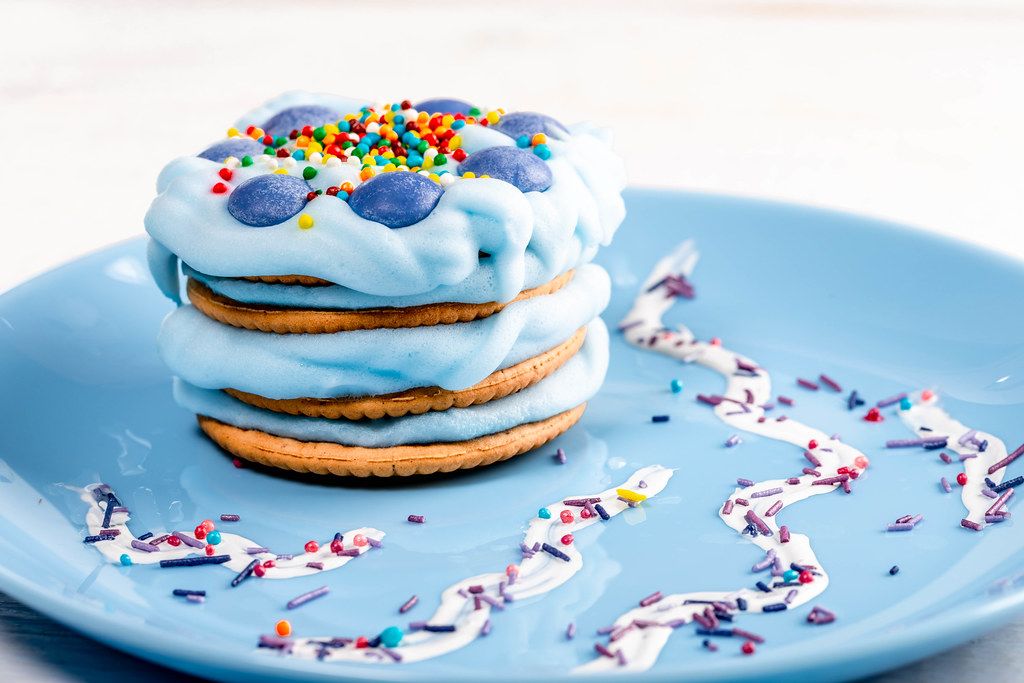 Kekse mit blauer Sahnecreme und bunten Streuseln auf einem verzierten Teller