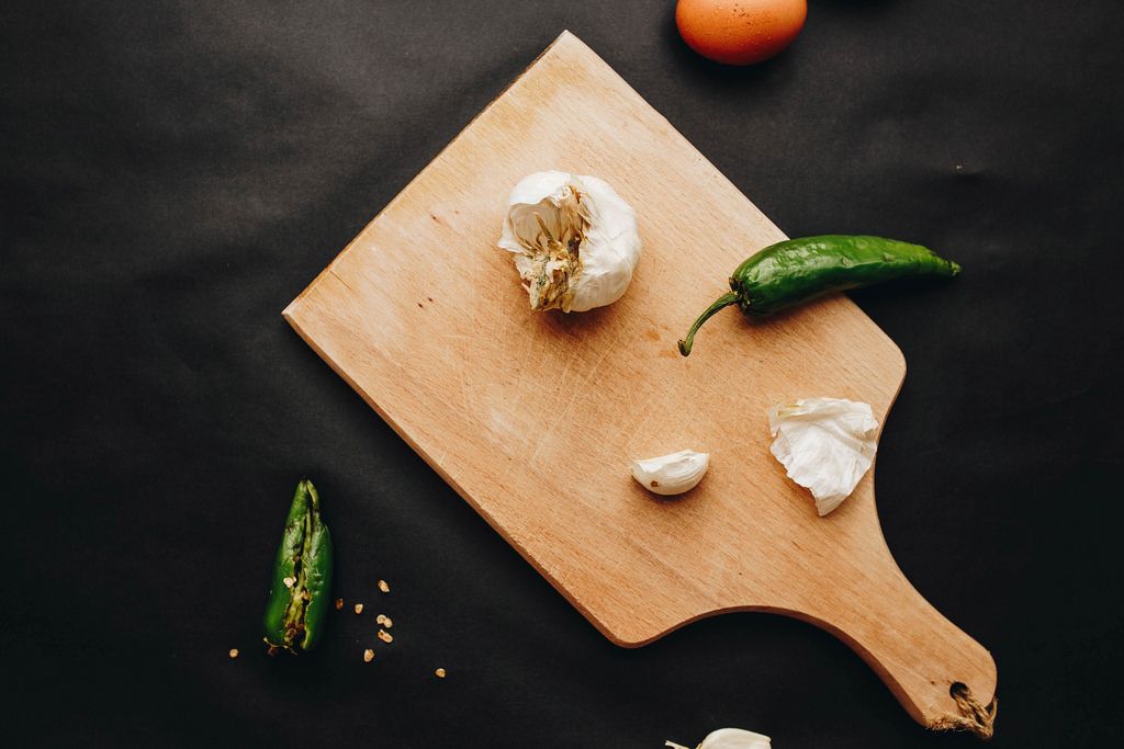 Kitchen flat lay with wooden board, chili peppers and garlic. Dark background
