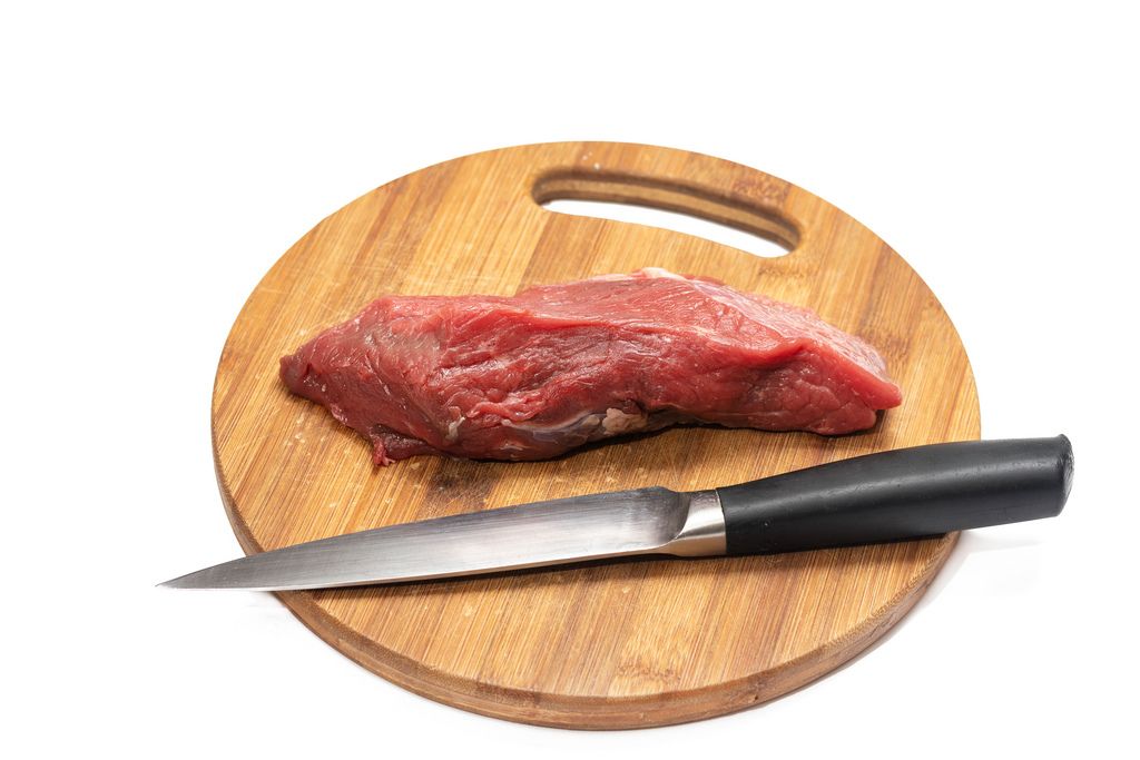 Kitchen knife and beef meat on the round wooden board