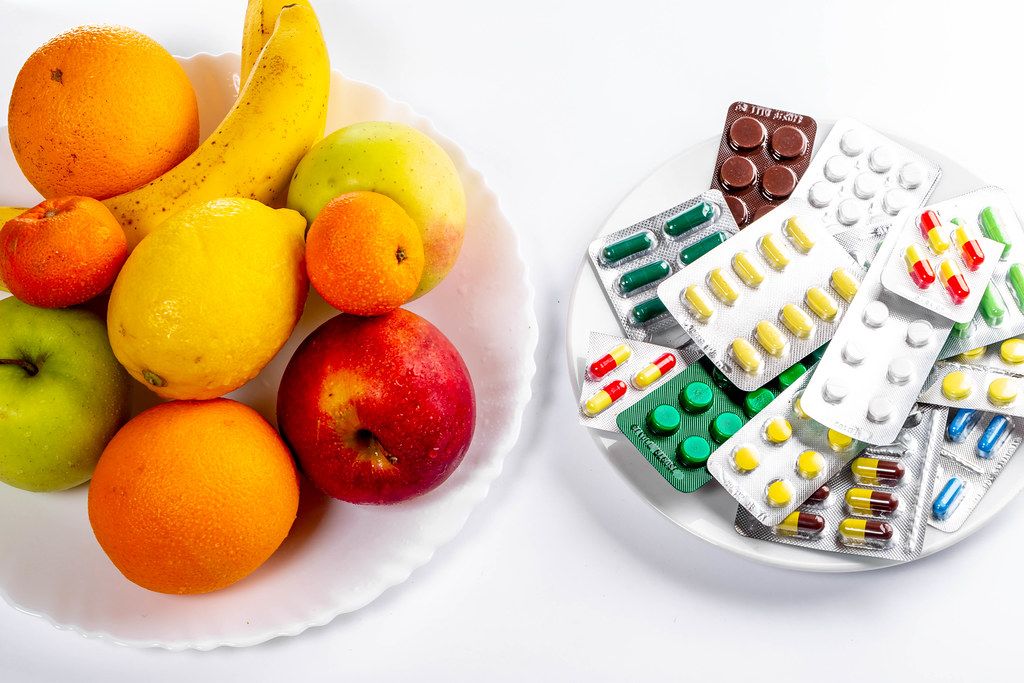 Konzeptbild zeigt Wahl zwischen gesunder Ernährung und Medikamenten-Behandlung, dargestellt mit Tabletten & frischen Früchte