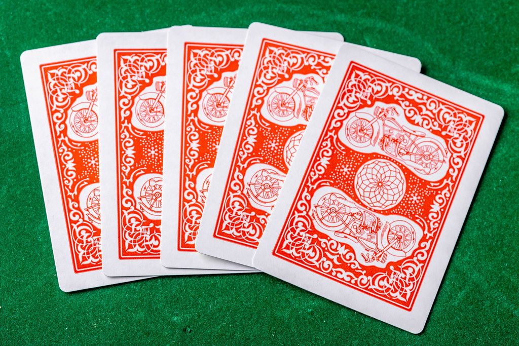 Konzeptbild zum Thema Glücksspiel zeigt fünf verdeckte Spielkarten, vor dem Start des Spiels, auf einer grünen Oberfläche