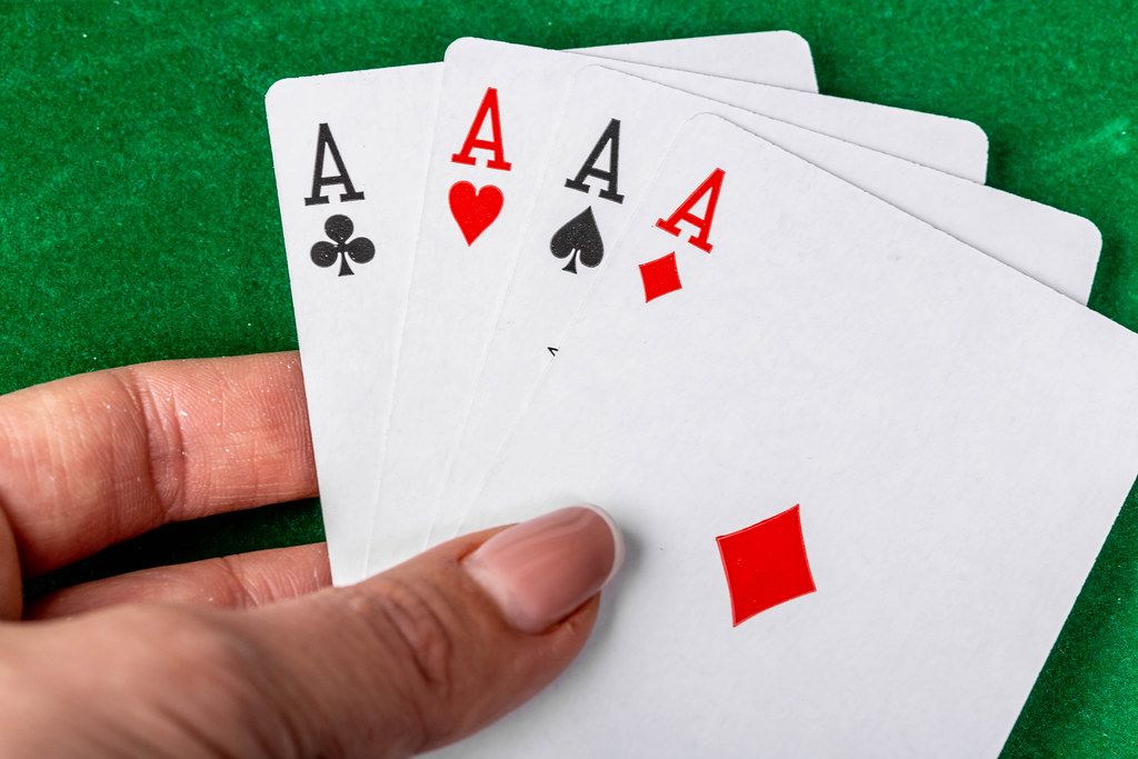 Konzeptbild zum Thema Poker spielen, mit vier Asse in einer Frauenhand, vor einem grünen Pokertisch