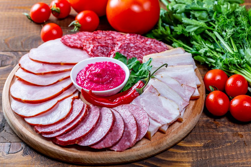 Küchenbrettchen mit aufgeschnittenen geräucherten Wurstwaren, Salami und Schinken mit pinker Sauce auf Holztisch