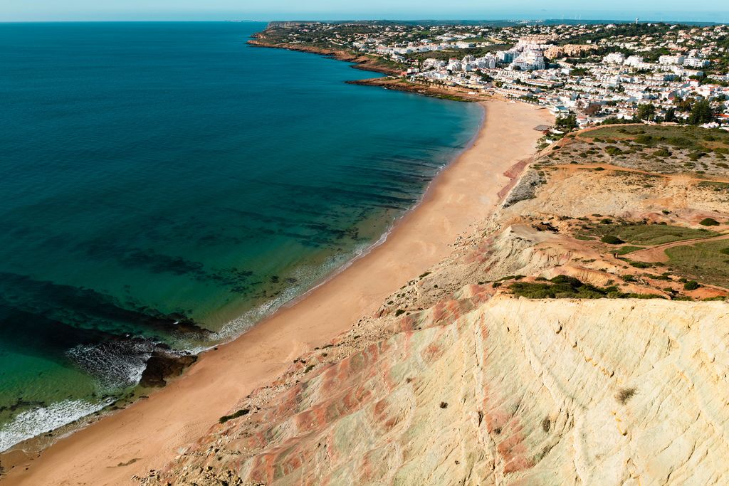 Küste bei Reserva da Luz, Portugal mit Klippen, Sandstrand, blauem Meer und weißer Stadt im Hintergrund