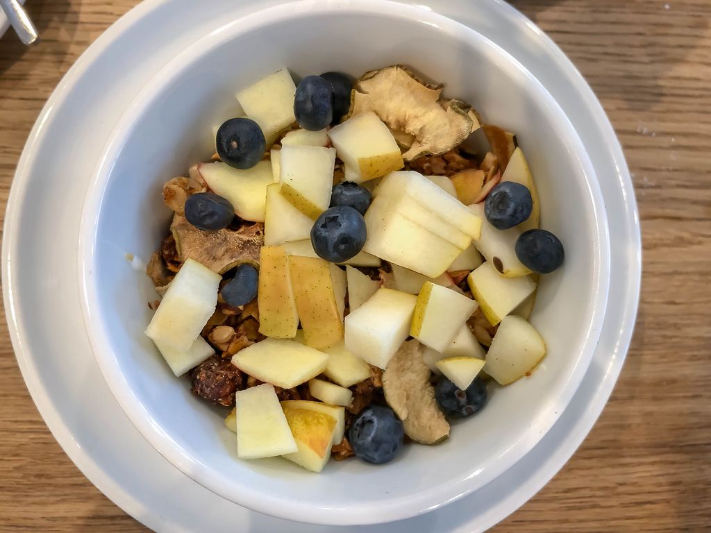 Leckeres Müsli zum Frühstück mit Blaubeeren, Birnen und Trockenobst in weißer Schüssel auf Holztisch