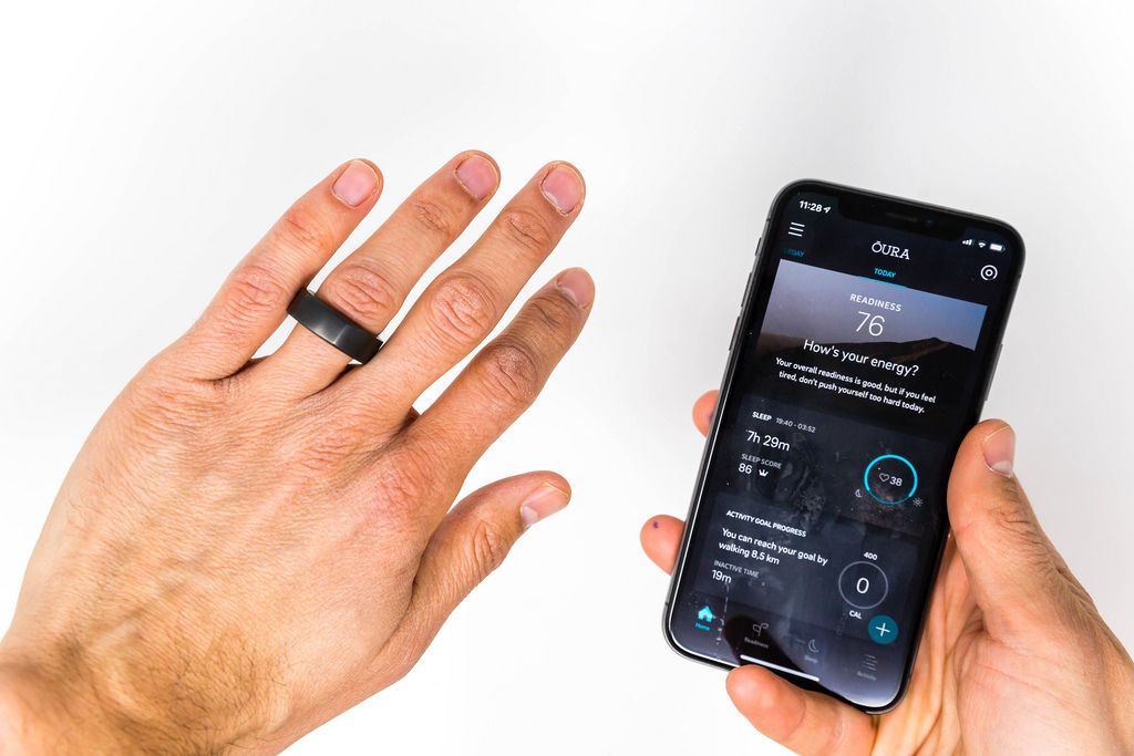 Left hand with Oura smart ring on finger, right hand shows phone with the Oura app´s energy and activity statistics
