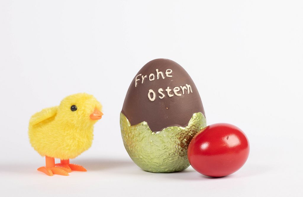 Little chicken and painted Easter egg with Frohe Ostern text