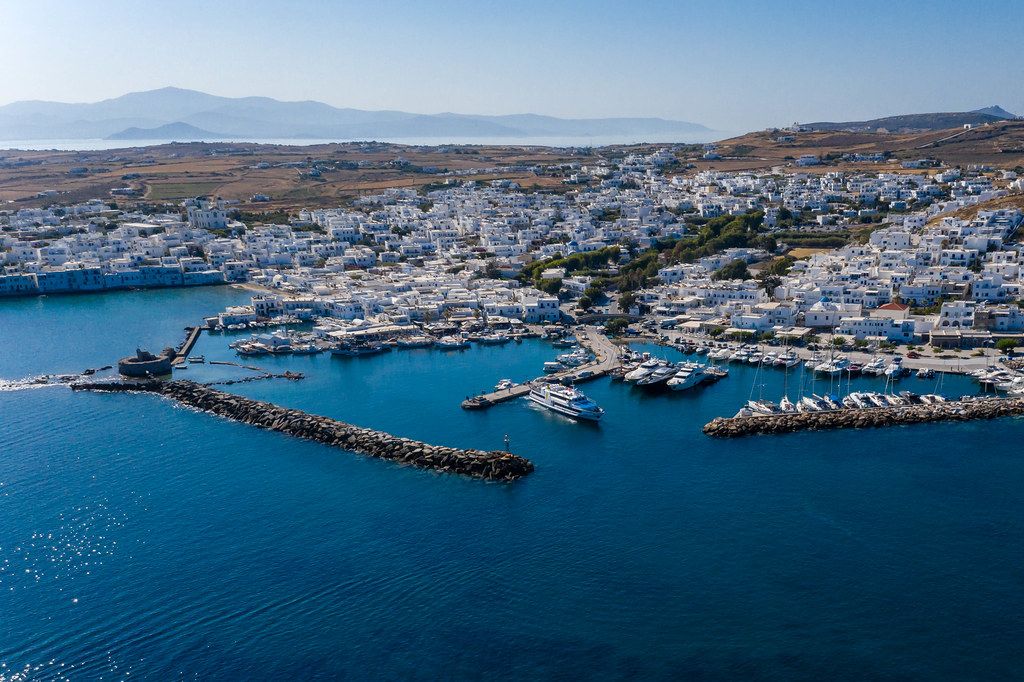 Luftaufnahme des Dorfs Naoussa auf der Kykladeninsel Paros, Griechenland, mit Hafen und alter Burgruine, in der Bucht Ormos Naousia