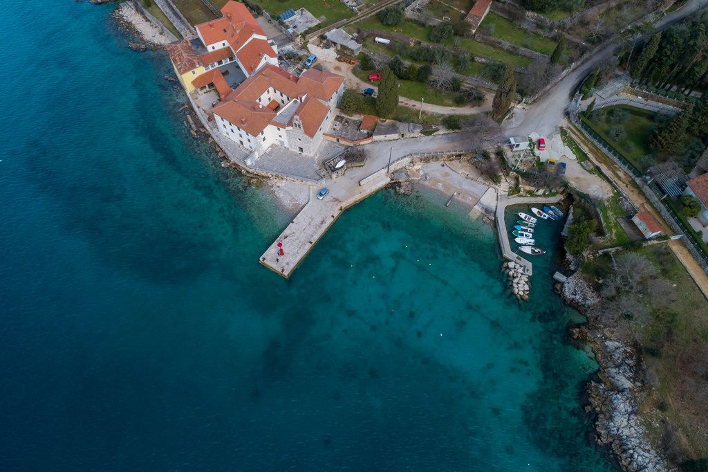 Luftaufnahme mit der Drohne von einer kleinen Bucht mit Bootssteg und Kloster an einem Kiesstrand
