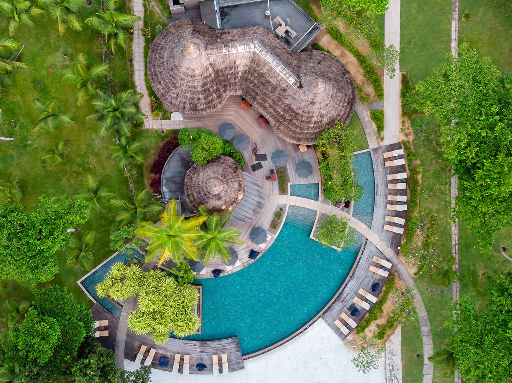 Luftaufnahme zeigt Terrassendeck und Cafés mit Bastdach an rundem Pool im Constance Ephelia Luxusresort auf Mahé, Seychellen