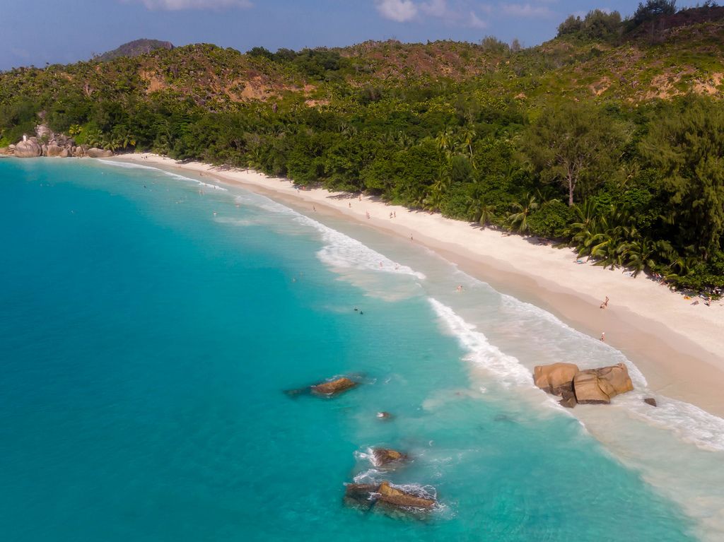 Luftaufnahme zeigt Urlauber in der Bucht Anse Lazio mit Granitfelsen im Indischen Ozean und weißem Sandstrand auf der Seychellen-Insel Praslin