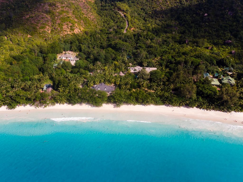 Luftbild der Gästehäuser im Palmenwald an der Bucht Anse Lazio auf Praslin (Seychellen), mit türkisblauem Meer und weißem Sandstrand