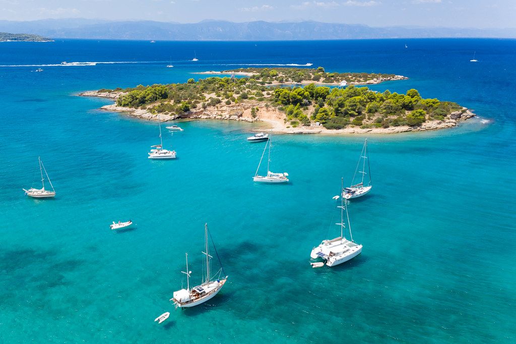 Luftbild von Segelbooten und Katamarane auf dem klaren blauen Wasser vor der unbewohnten griechischen Insel Chenesar
