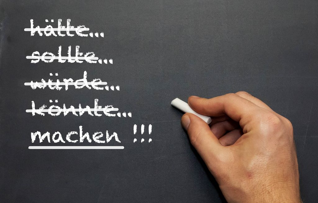 Machen!: Mann schreibt mit Kreide verschiedene konjunktive Verben auf eine Tafel - Nahaufnahme