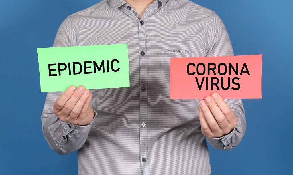 Man holding a green banner with a word epidemic and red banner with Coronavirus text on blue background