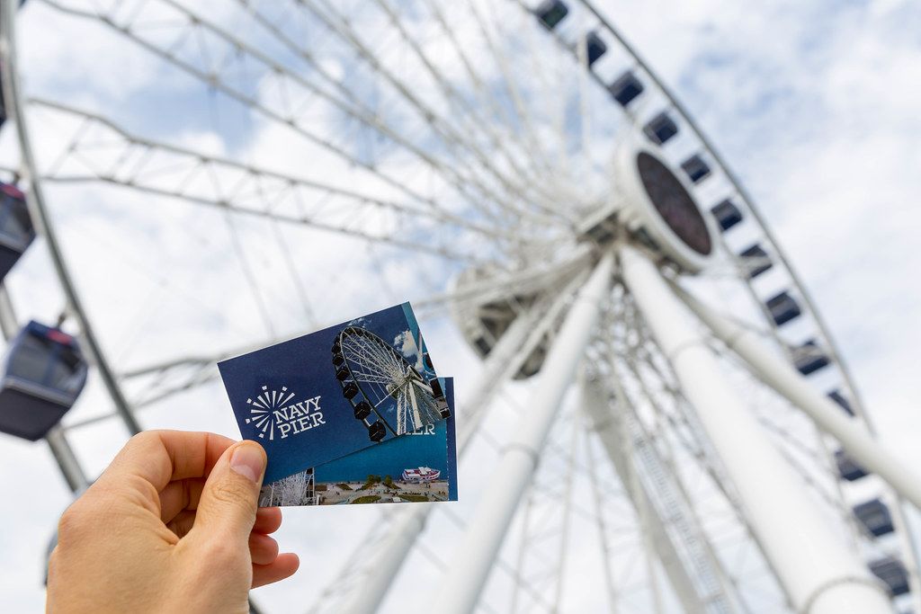 Man holds Navy Pier tickets in his hand, with a big Ferris wheel in the background