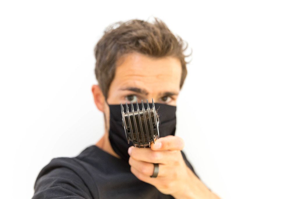 Man wearing non-medical face mask shows the comb attachment of the Philips QC5115/15 hair clipper. Portrait with white background