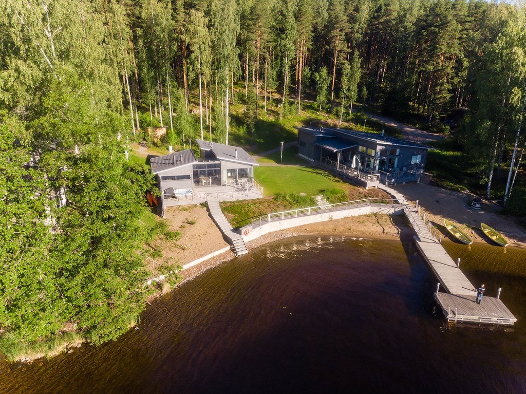Mann auf einem Holzsteg schießt ein Drohnenfoto von der Villa Jolla an Finnlands längstem See Päijänne, mit nordischem Wald im Hintergrund