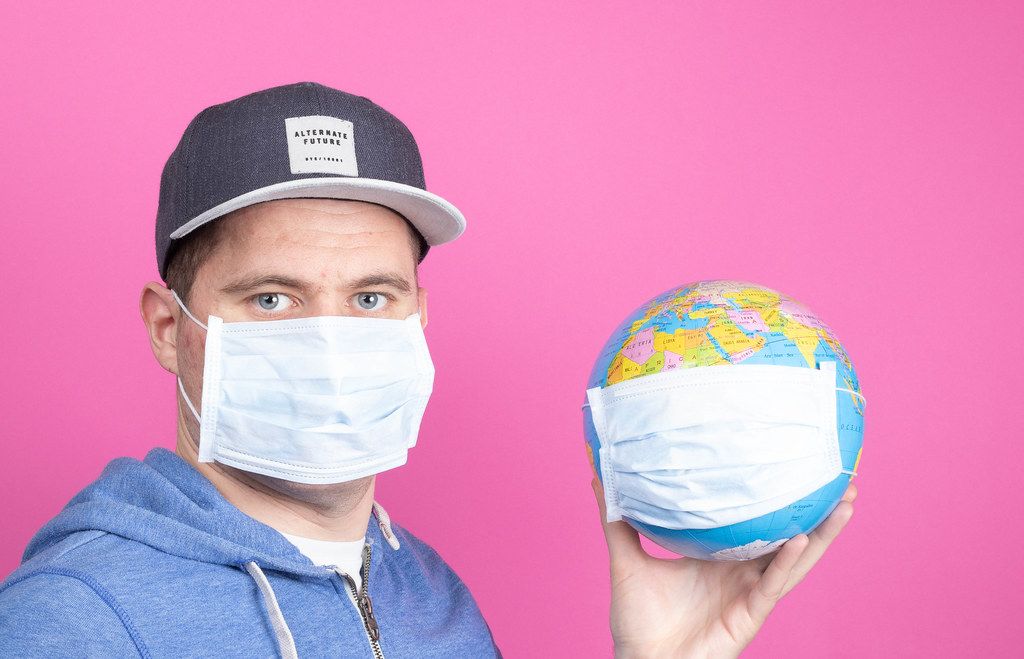 Mann mit Gesichtsmaske hält eine Weltkugel mit Gesichtsmaske auf pinkem Hintergrund