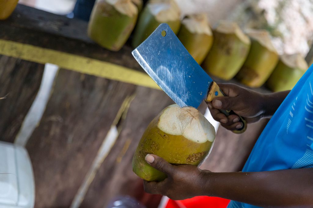 Mann mit Hackbeil schneidet eine grüne Kokosnuss an einer Strandbar am Anse Source d'Argent auf La Digue, Seychellen