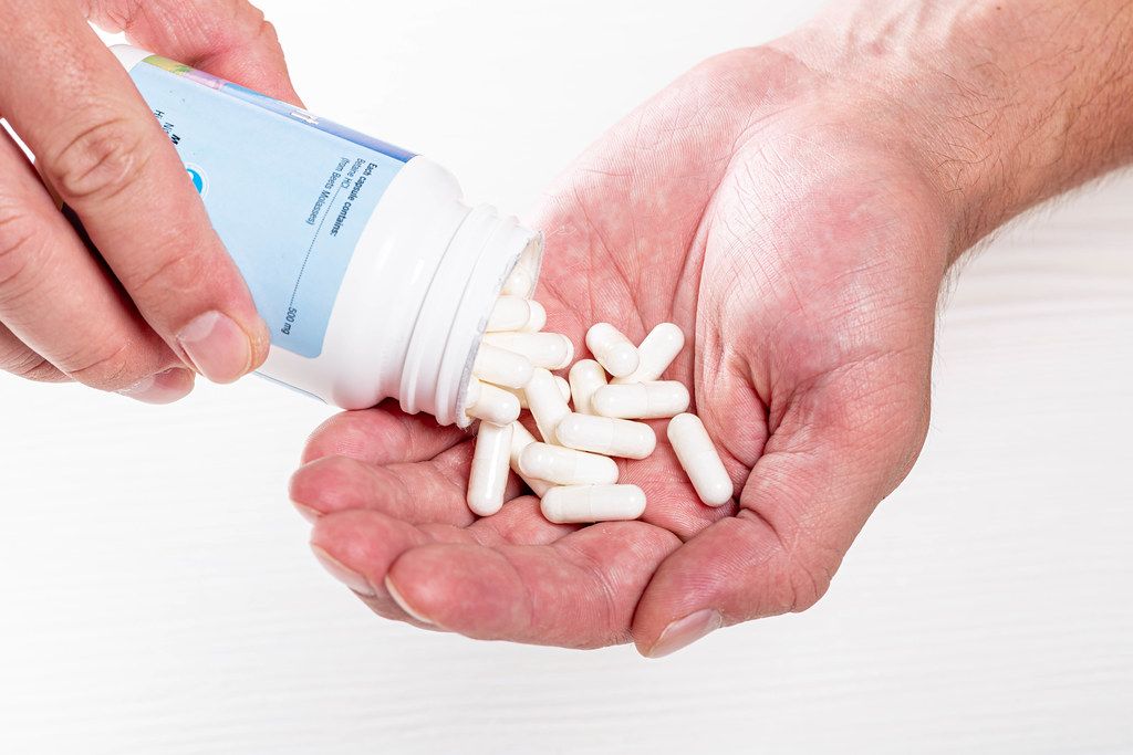 Mann schüttet medizinische Tabletten aus Dose in Handfläche vor weißem Hintergrund