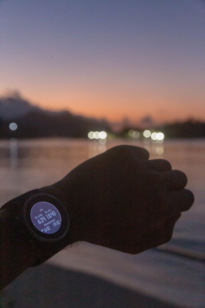 Männerarm mit Garmin Fenix 5S Smartwatch, die Sonnenaufgang, Sonnenuntergang und Dämmerung im Constance Ephelia Resort auf Mahé, Seychellen, anzeigt