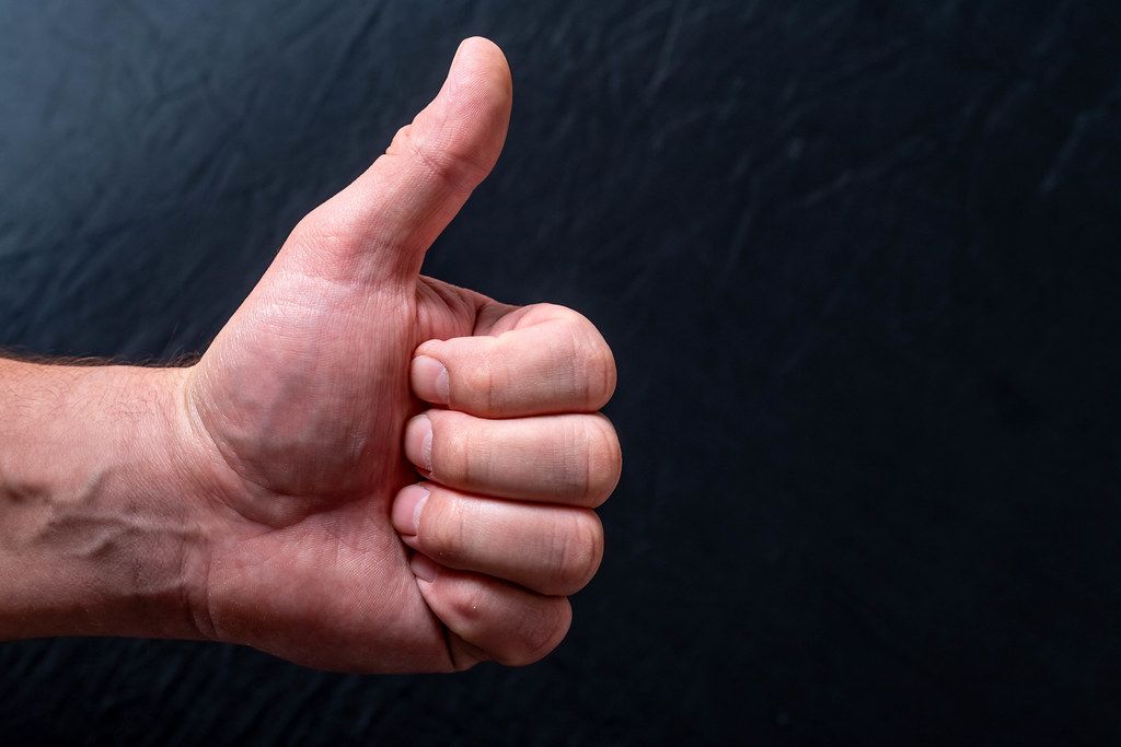 Man's hand showing thumb up - like sign on black background. Concept positive assent (Flip 2019)
