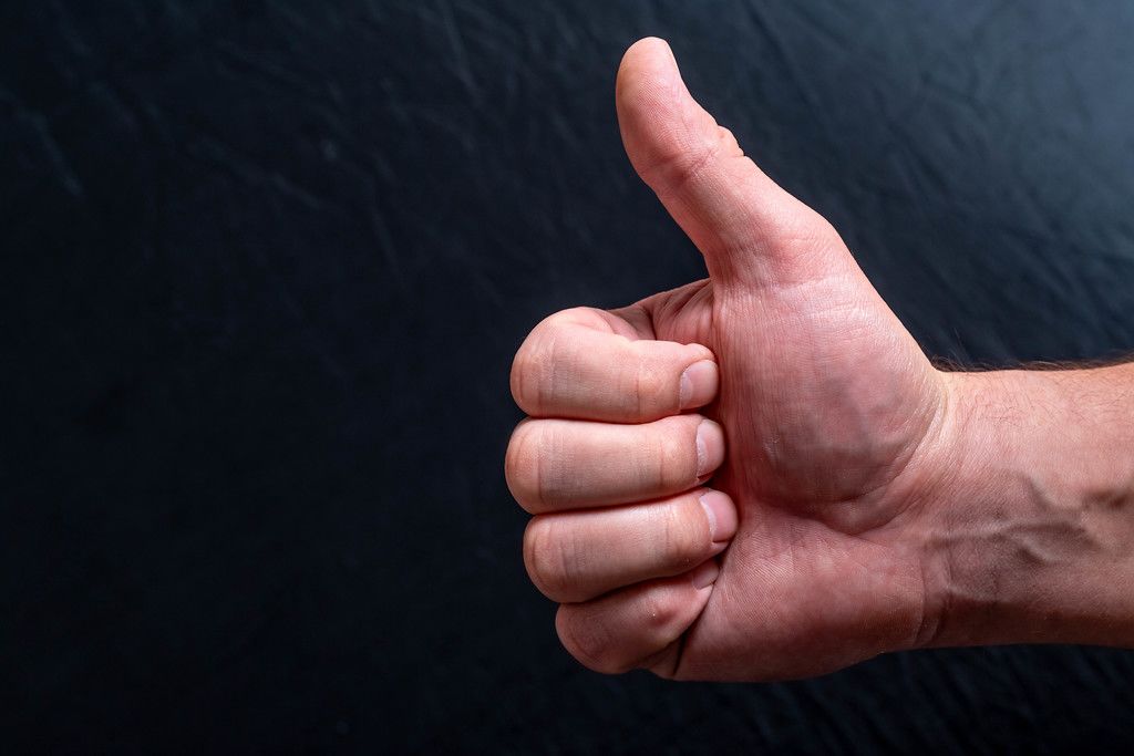 Man's hand showing thumb up - like sign on black background. Concept positive assent