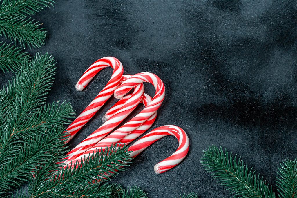 Many Christmas candy canes with Christmas tree branches on a black background (Flip 2019)