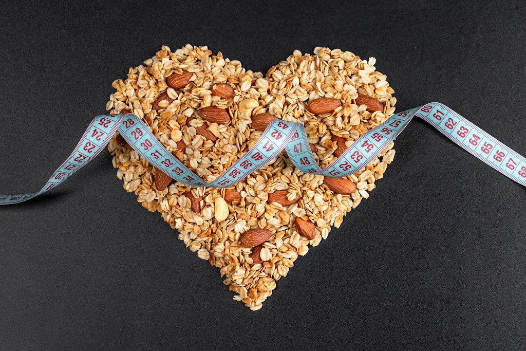 Measuring tape on a heart made of oatmeal with almonds on a black background. Nutritional concepts
