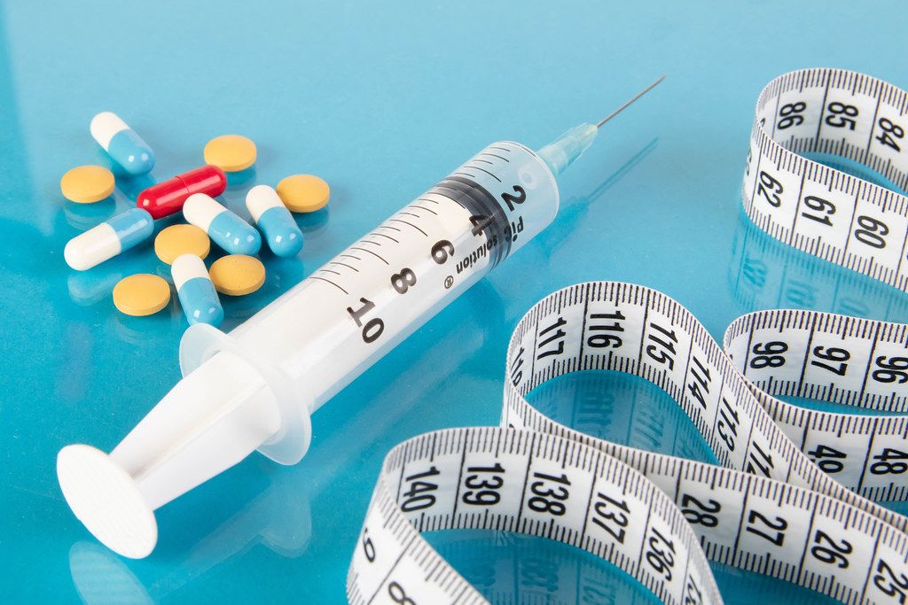 Medical syringe, pills and tape measure on blue background