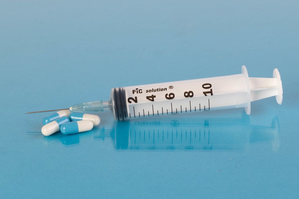 Medical syringe with pills on blue background