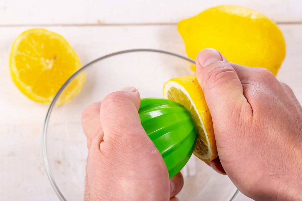 Menschliche Hände nutzen die grüne Saftpresse, um Saft aus der halbierten Zitrone zu pressen