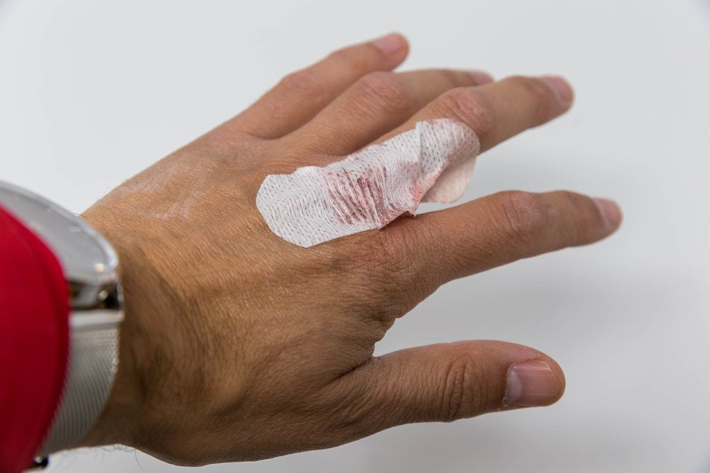 Minor injury: man's hand with white plaster and wound with blood on the middle finger, close-up