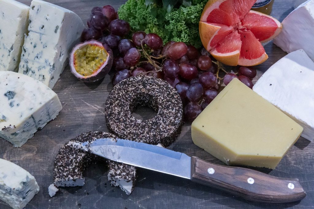 Mould cheese, cream cheese and hard cheese lies with a knife on a wooden surface next to fresh fruit