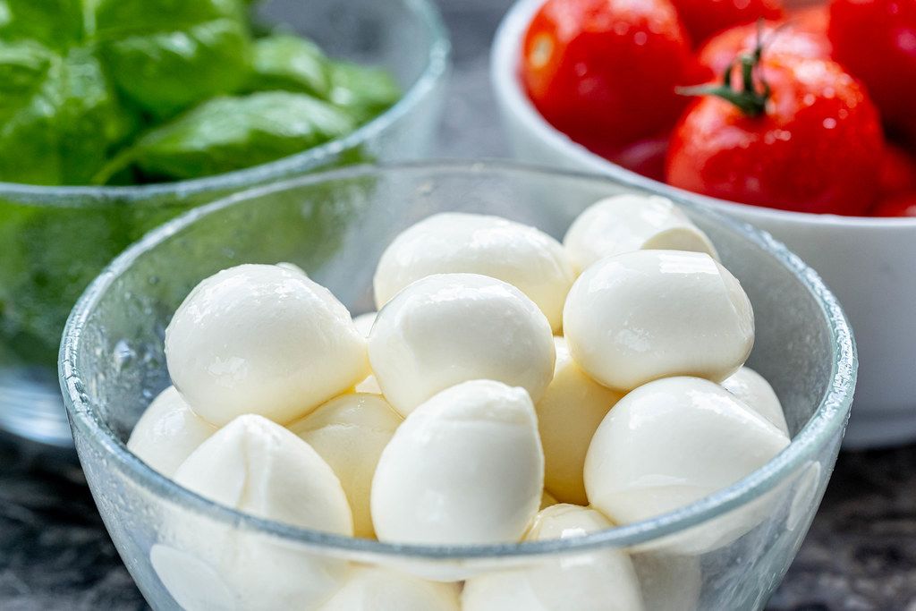 Mozzarella cheese, red cherry tomatoes and fresh Basil leaves in bowls ...
