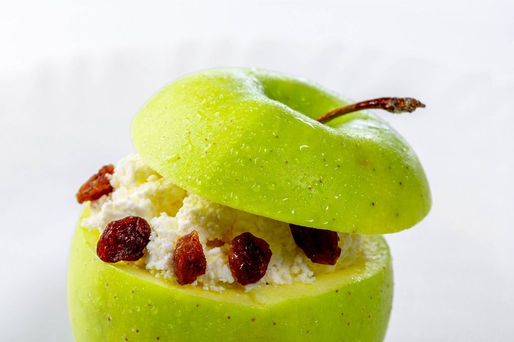 Nahaufnahme eines frischen, grünen Apfels, gefüllt mit Hüttenkäse und Rosinen, vor weißem Hintergrund