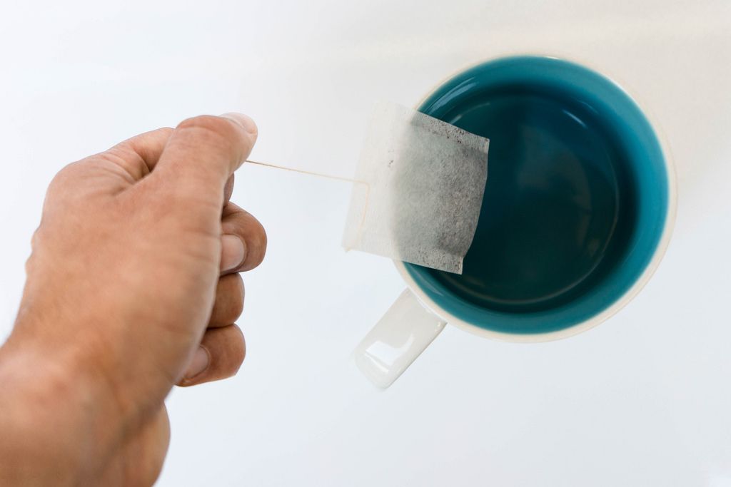 Nahaufnahme eines Teebeutels von einer Hand gehalten in einer Tasse auf weißem Hintergrund
