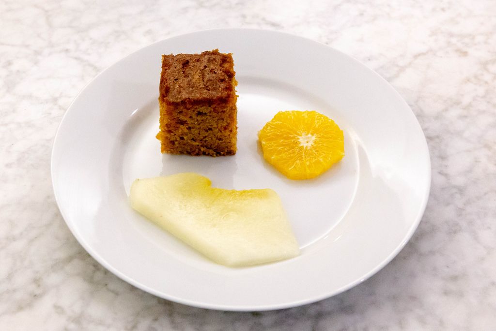Nahaufnahme - Karottenkuchen auf weißem Teller mit einer Scheibe Orange und Honigmelone