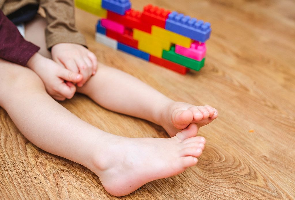 Nahaufnahme von Kinderbeinen auf dem Boden neben Spielzeug