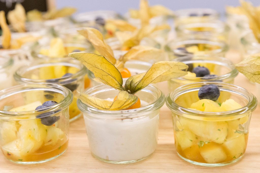 Nahaufnahme von kleinen Frühstückssnacks in Gläsern, mit Klebreis, Kokosmilch und Sesamkernen und eingelegte Ananas in süß-sauer Sauce