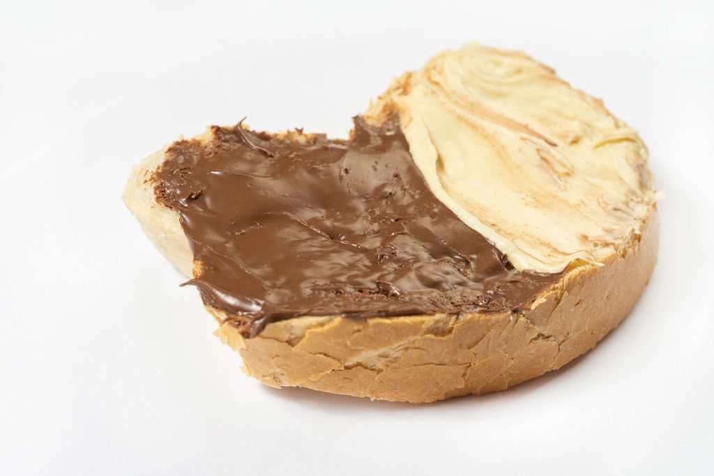 Nahaufnahme von Stück Brot mit Aufstrich aus heller und dunkler Schokolade vor weißem Hintergrund