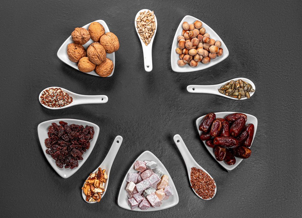 Nuts, seeds, dried dates and candied fruits are arranged in a circle on a black background. Top view