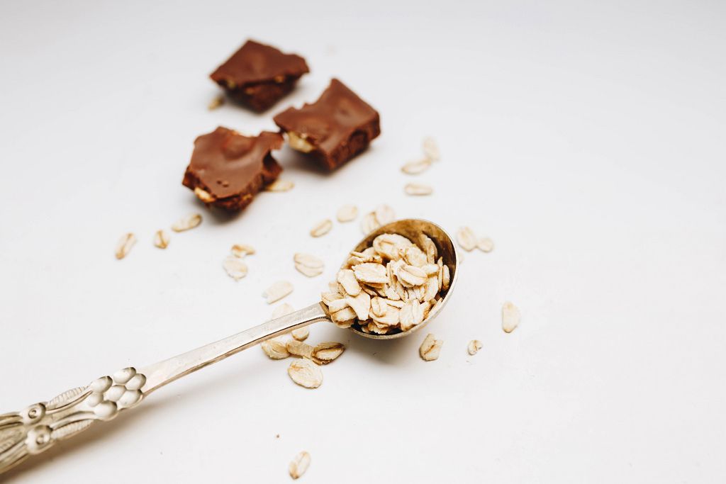 Oat flakes in a vintage spoon and chocolate pieces in the background. White background.