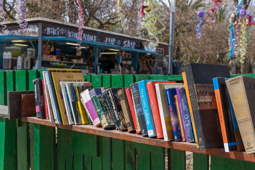 Öffentliche Bücherei zum Tauschen und Mitnehmen auf einem Regalbrett an einem grünen Gartenzaun im spanischen Barceloneta Park in Barcelona