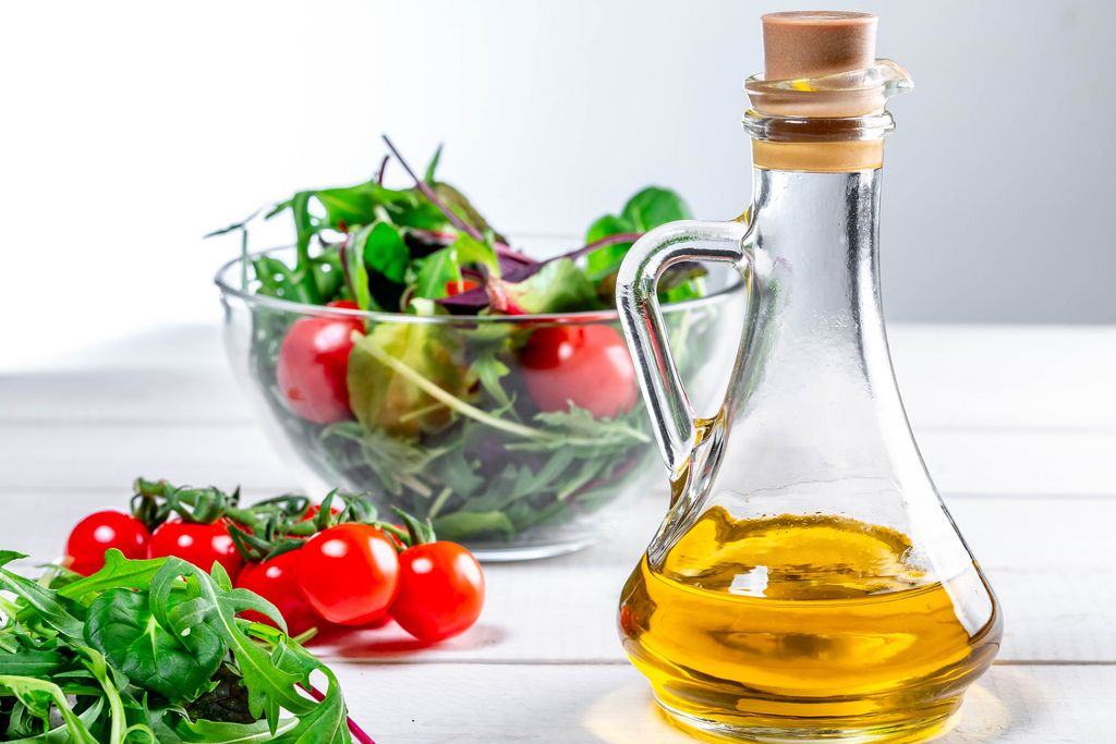 Olivenöl in Karaffe vor Zutaten für einen gesunden Salat, in einer Glasschale auf einem Holztisch