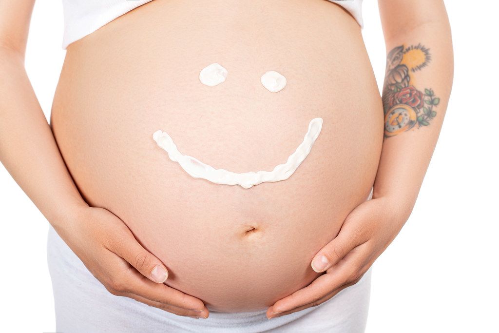 On a pregnant belly a painted smile. The concept of joy, cheerful expectation of a baby