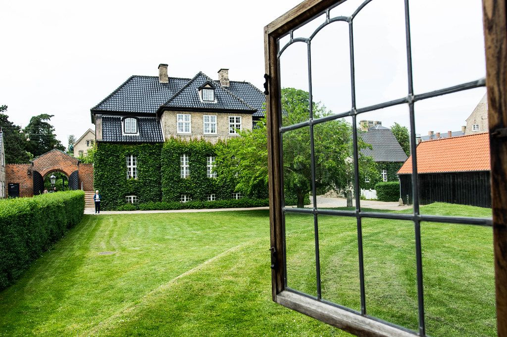 Open window looking out to a green grass field and elegant Danish house