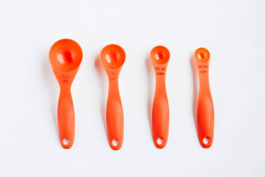 Orange plastic measuring spoons on white background.